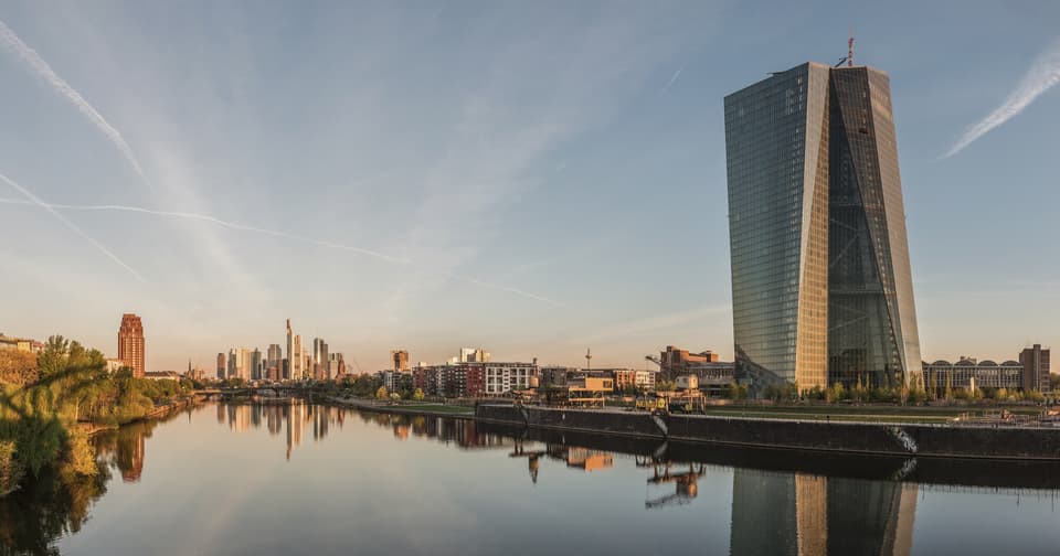 The European Central Bank tower on the River Main in Frankfurt, with the city skyline behind at dawn.
