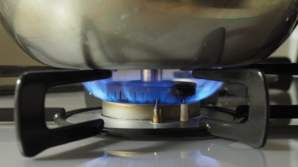 A blue gas flame burning under a stainless steel pot on a domestic hob.