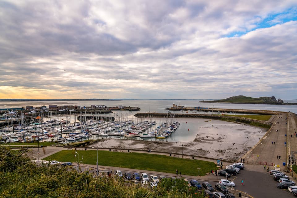 Howth harbour and marina seen from above, with Ireland's Eye offshore under a cloudy sky.