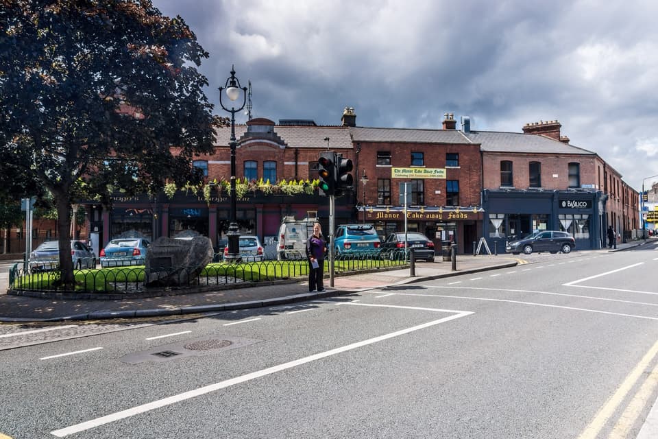 The junction of Manor Street in Stoneybatter, with red-brick shopfronts and a small railed green.